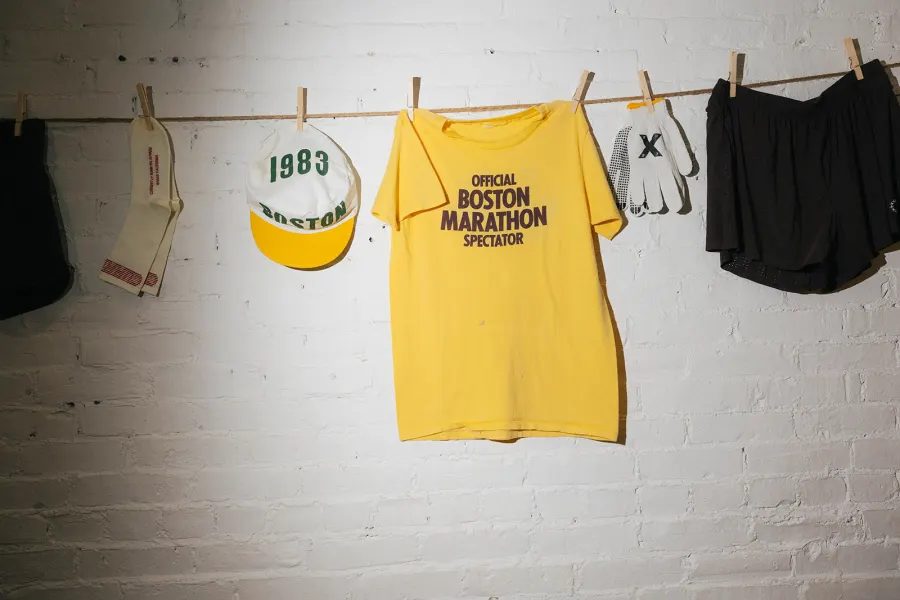 A yellow Official Boston Marathon Spectator tee pegged to a clothesline between socks, a cap, gloves and shorts