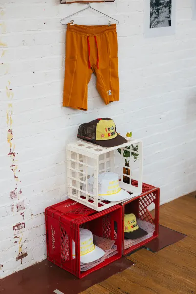 Orange running shorts on a wire hanger above stacked red and white milk crates holding trucker caps