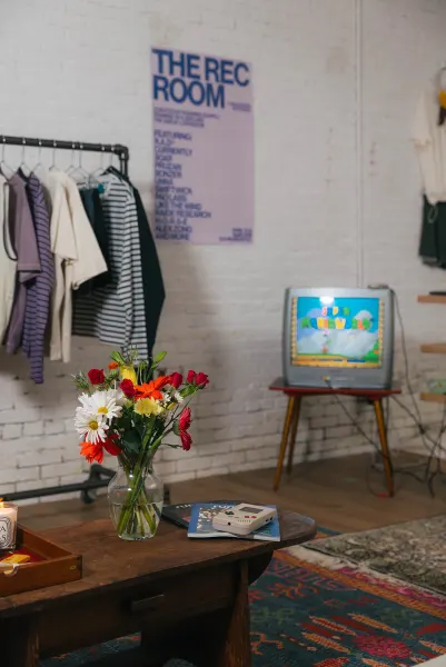 The lilac Rec Room poster on brick beside a CRT television playing Super Mario World, flowers on a wooden table