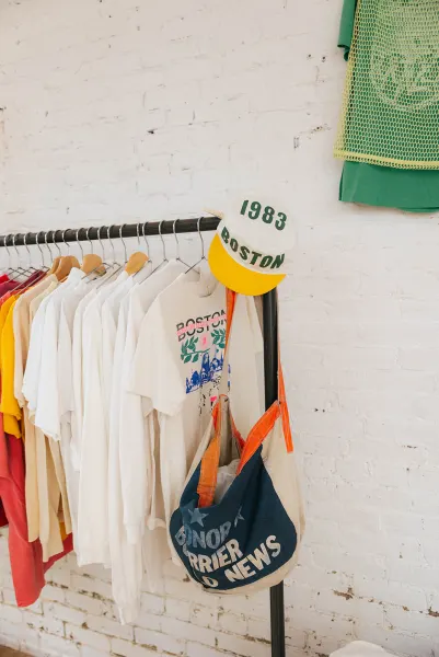 A rack of faded vintage Boston Marathon tees with a 1983 painters cap and a canvas tote hung on the end