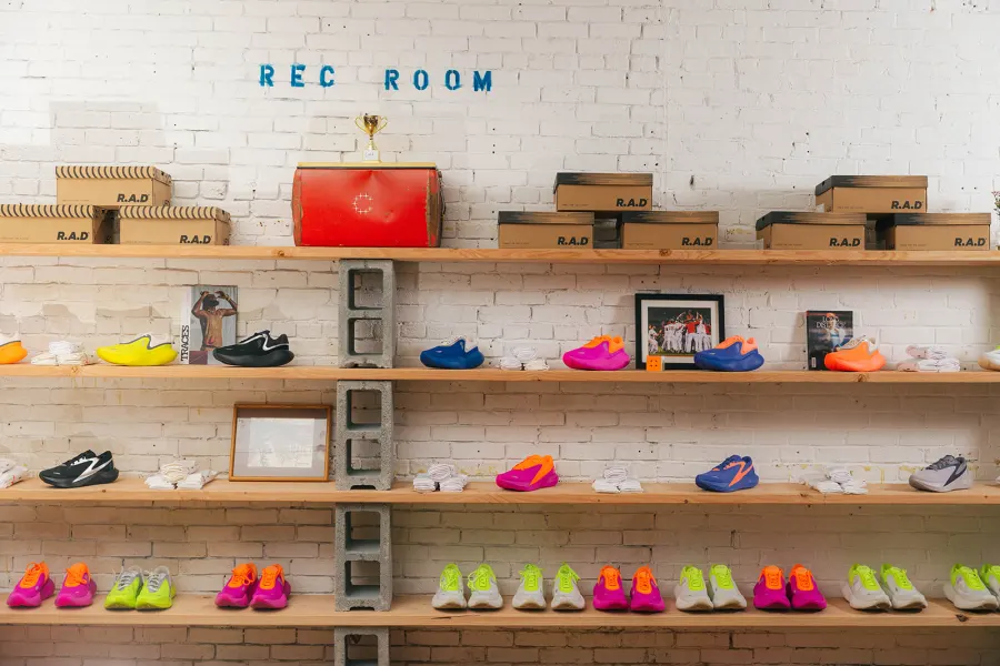 Scaffold-board shelves of R.A.D shoes and boxes against white brick, a trophy on top