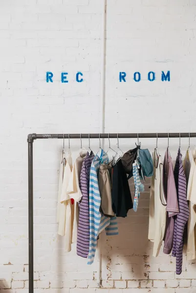 REC ROOM stencilled in blue on a white brick wall above a pipe rack of striped running tops